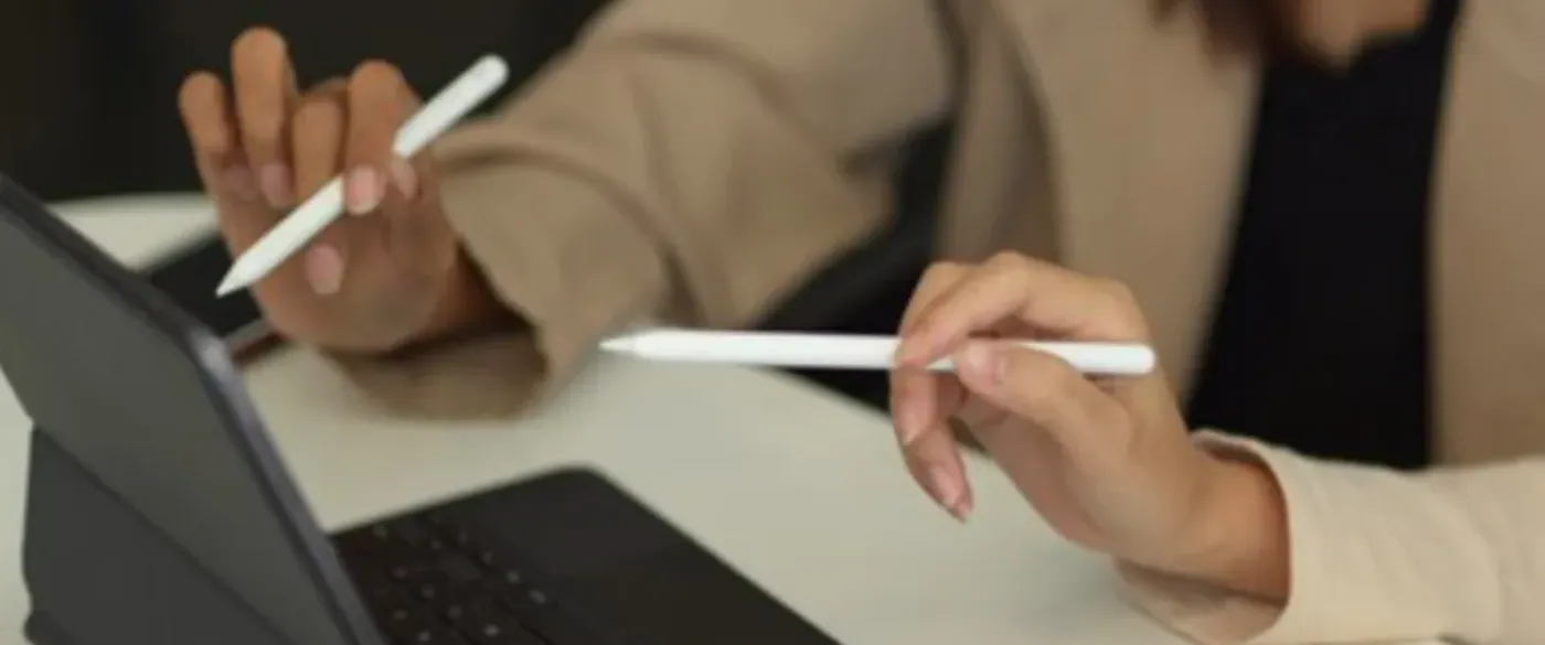 two women sitting at desk looking at laptop, only hands visible